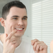 Homme souriant devant un miroir en appliquant une bande de blanchiment dentaire sur ses dents.
