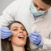 Dentiste en blouse blanche examinant la bouche d’une patiente souriante