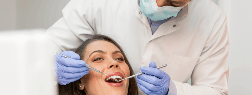 Dentiste en blouse blanche examinant la bouche d’une patiente souriante