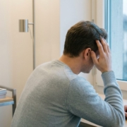 Personne assise près d'une fenêtre, main à la tempe, douleur du visage