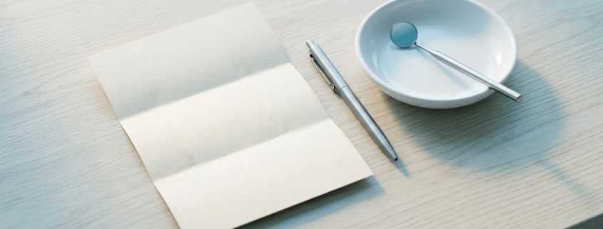 Document plié, stylo et miroir dentaire disposés sur un plan en chêne